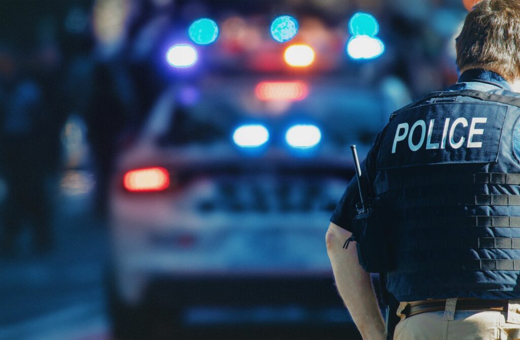 Police officer stands in front of car with lights on