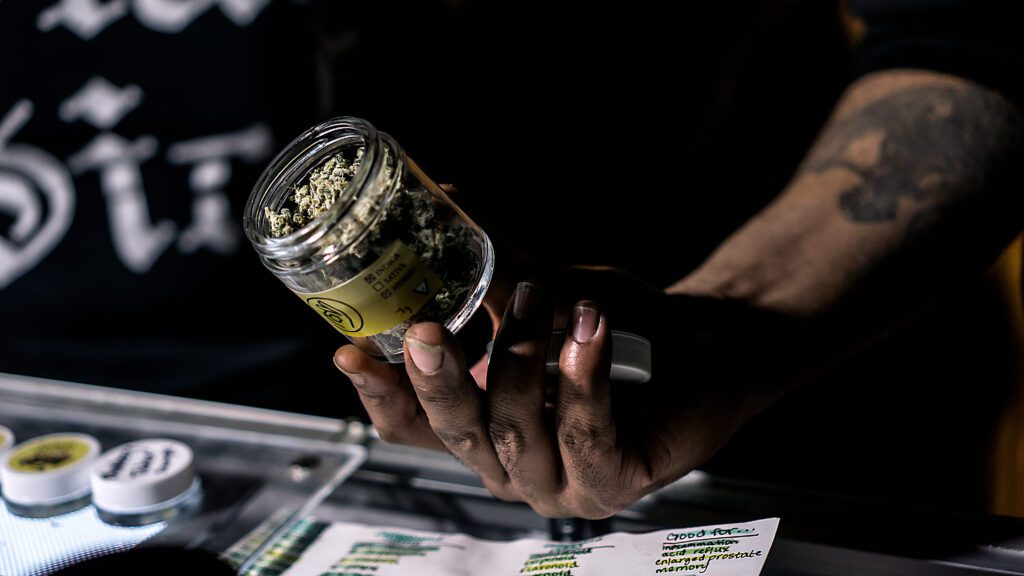 A Vendor Showing Off A Jar Of Cannabis Flowers